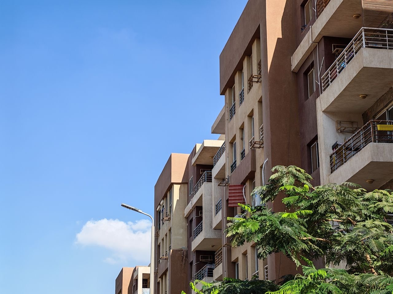 about-us Urban apartment building against a bright blue sky with foliage in the foreground.